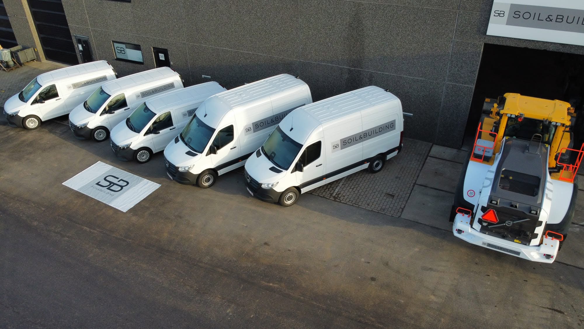 Vloot witte Soil & Building bedrijfswagens geparkeerd voor het hoofdkantoor, inclusief bestelwagens en een kraanvoertuig
