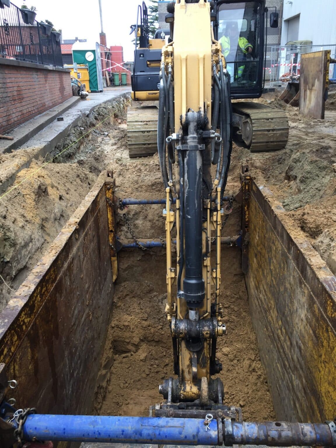 Rupsgraafmachine in beschoeide sleuf tijdens bodemsanering voor Belgomine, uitgraving 6 meter diep tussen woning en opslagplaats