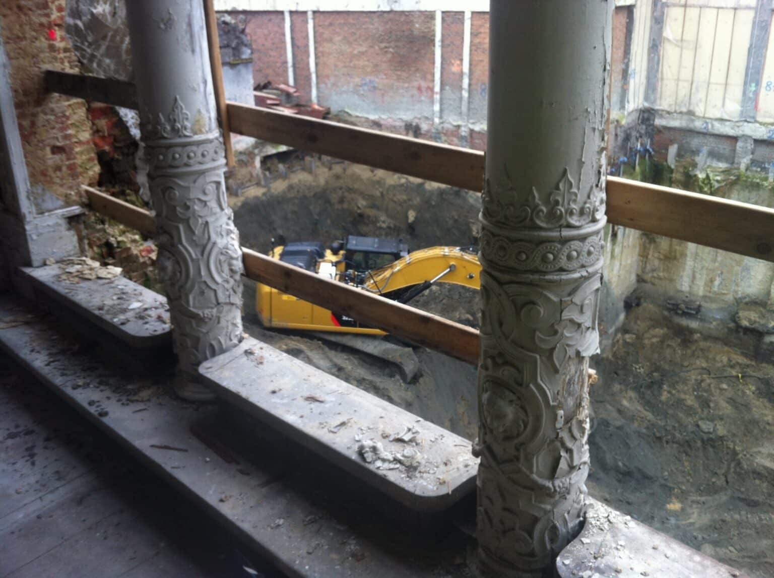 Versierde gietijzeren kolommen in het historische De Post-gebouw op de Korenmarkt in Gent, met een gele minikraan