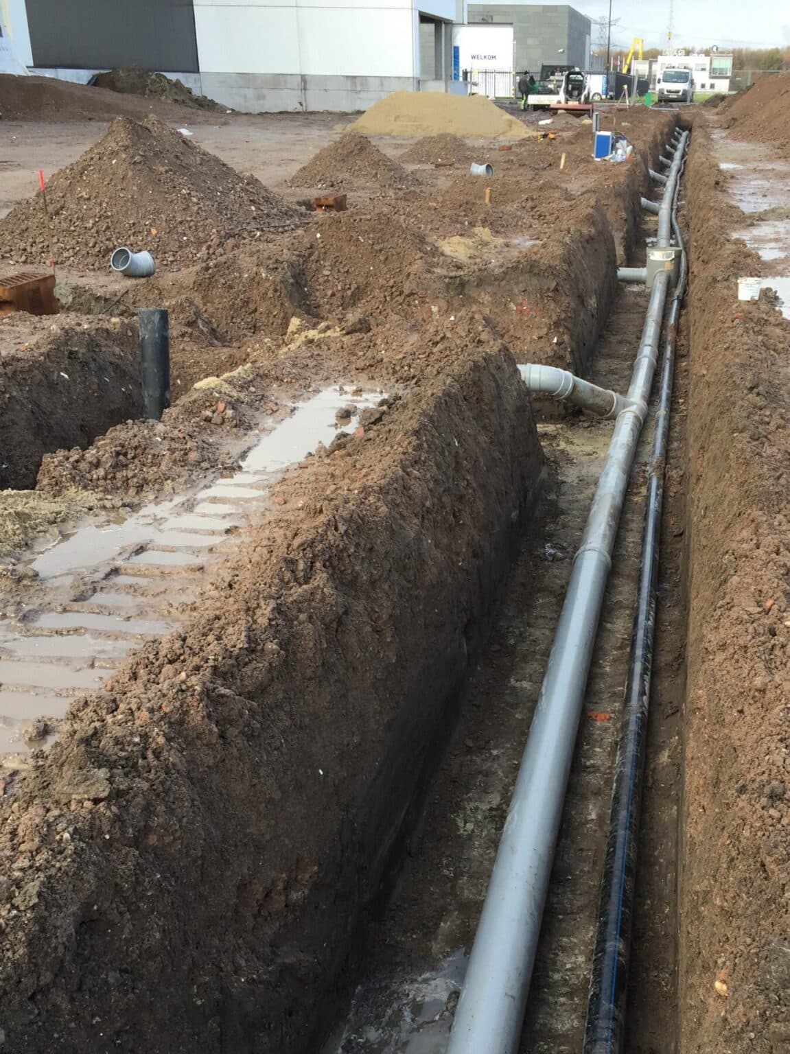 Uitgegraven sleuf met PVC-rioleringsbuizen voor afvoer van regenwater en vuilwater op de werf van logistiek centrum Yusen Logistics