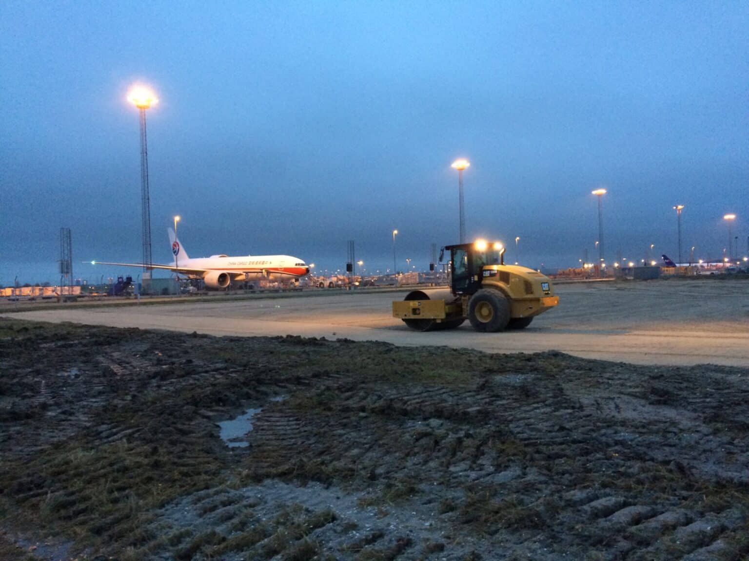Wals verdicht de ondergrond op de luchthaven van Kopenhagen bij zonsondergang, met een China Eastern vliegtuig op de achtergrond
