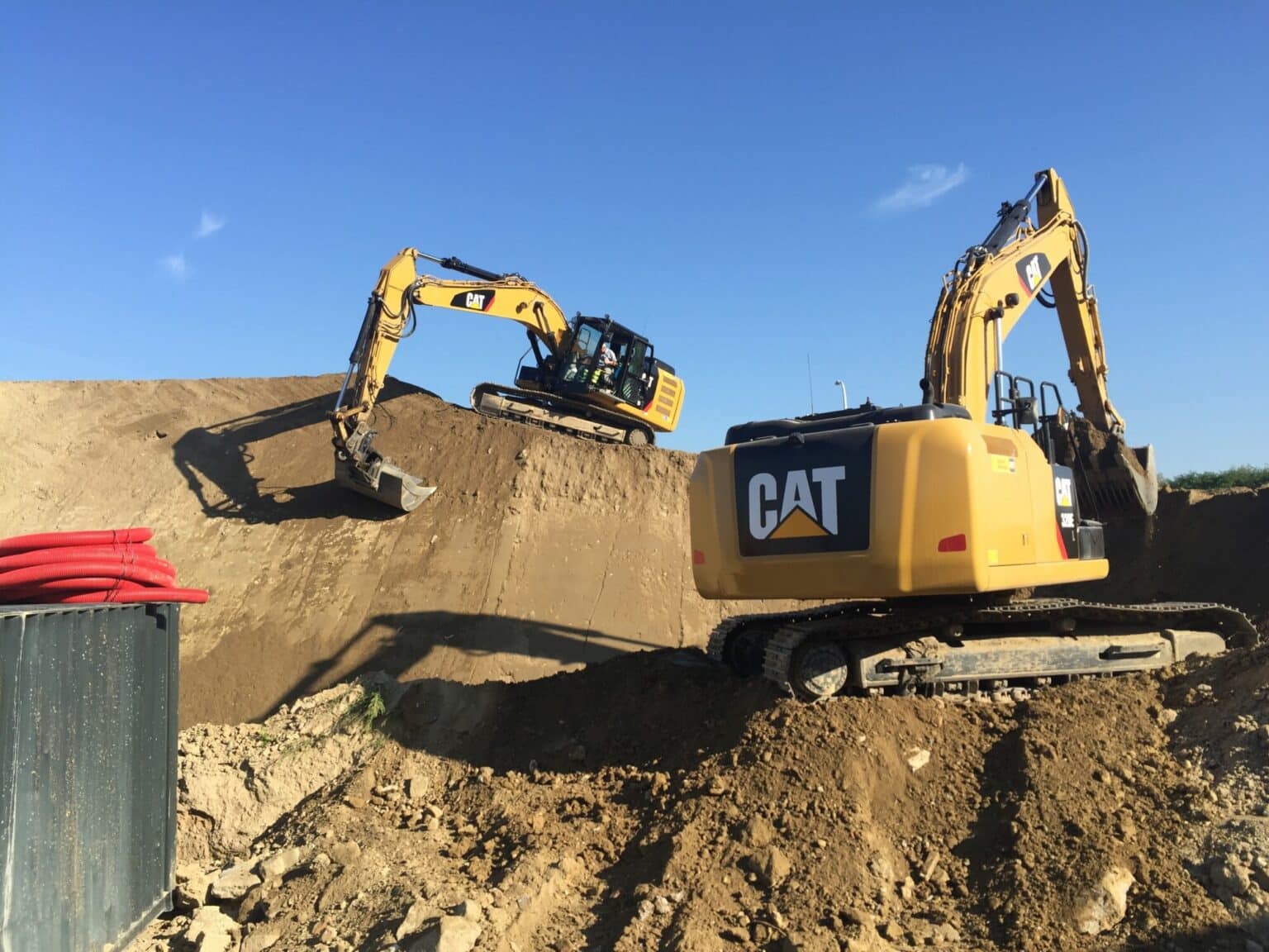 Twee gele CAT rupsgraafmachines graven vervuilde grond uit tijdens bodemsaneringsproject voor DHL hub in Zaventem