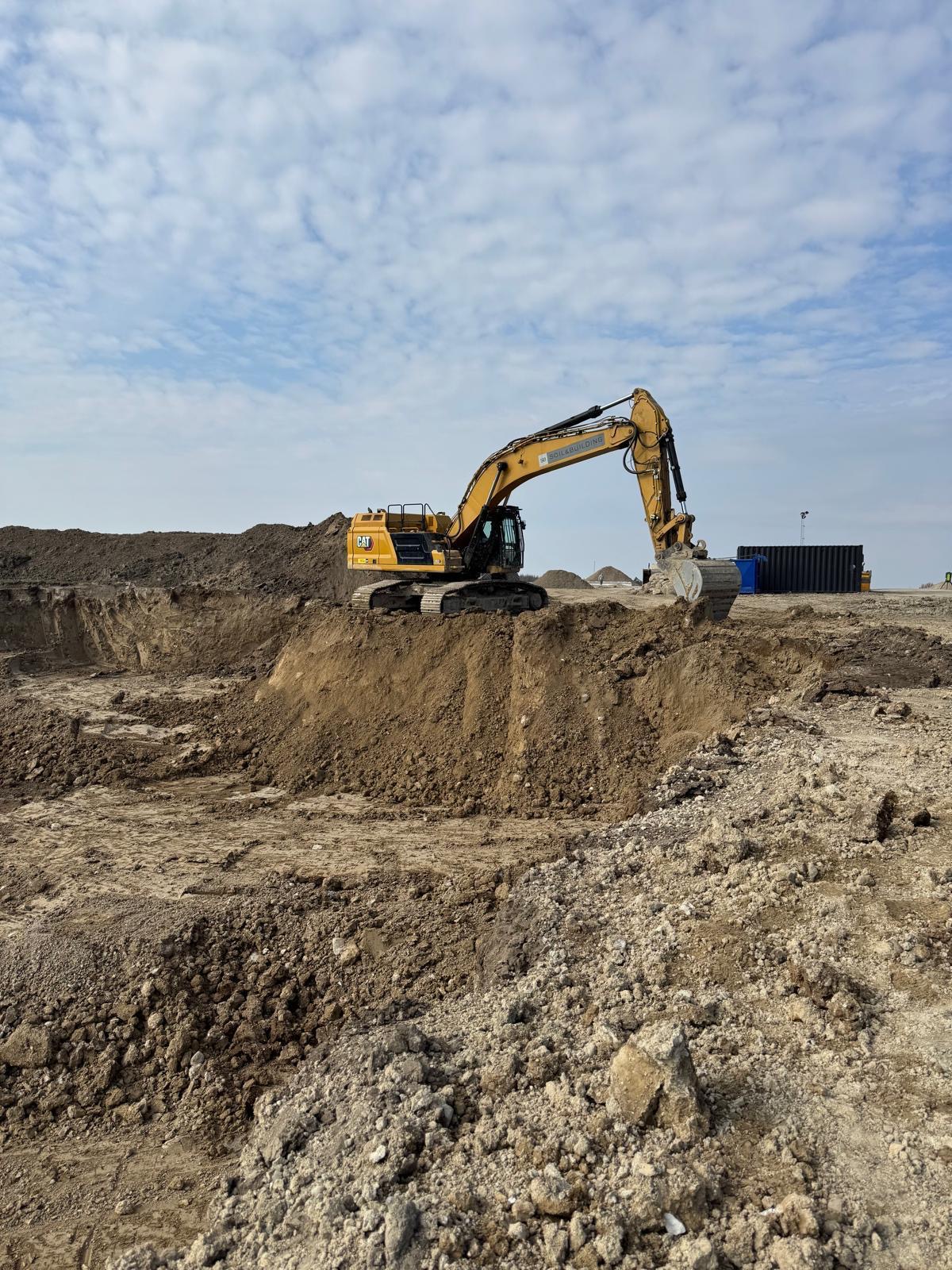 Gele Caterpillar rupsgraafmachine van Soil & Building in actie op een grote bouwput tijdens grondwerken