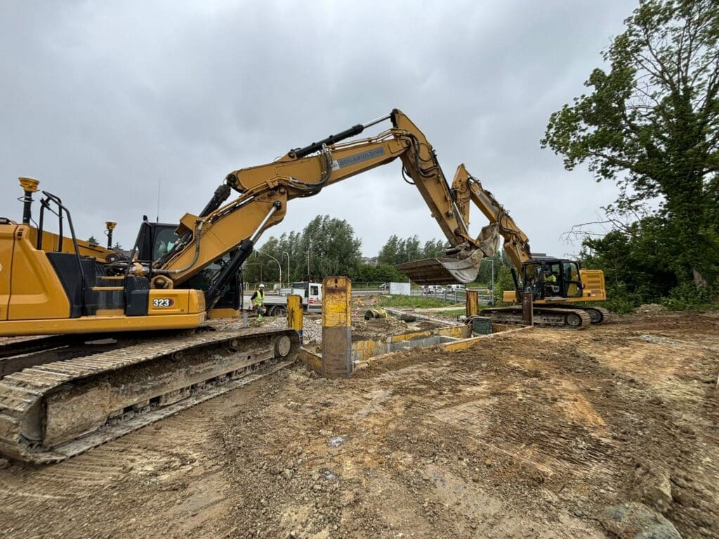 Twee gele rupsgraafmachines van Soil & Building actief op een bouwwerf tijdens grondwerken, met graafbak en bouwput zichtbaar