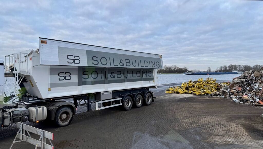 Volumekipper met belettering van Soil & Building aan de kade, klaar om grond af te voeren