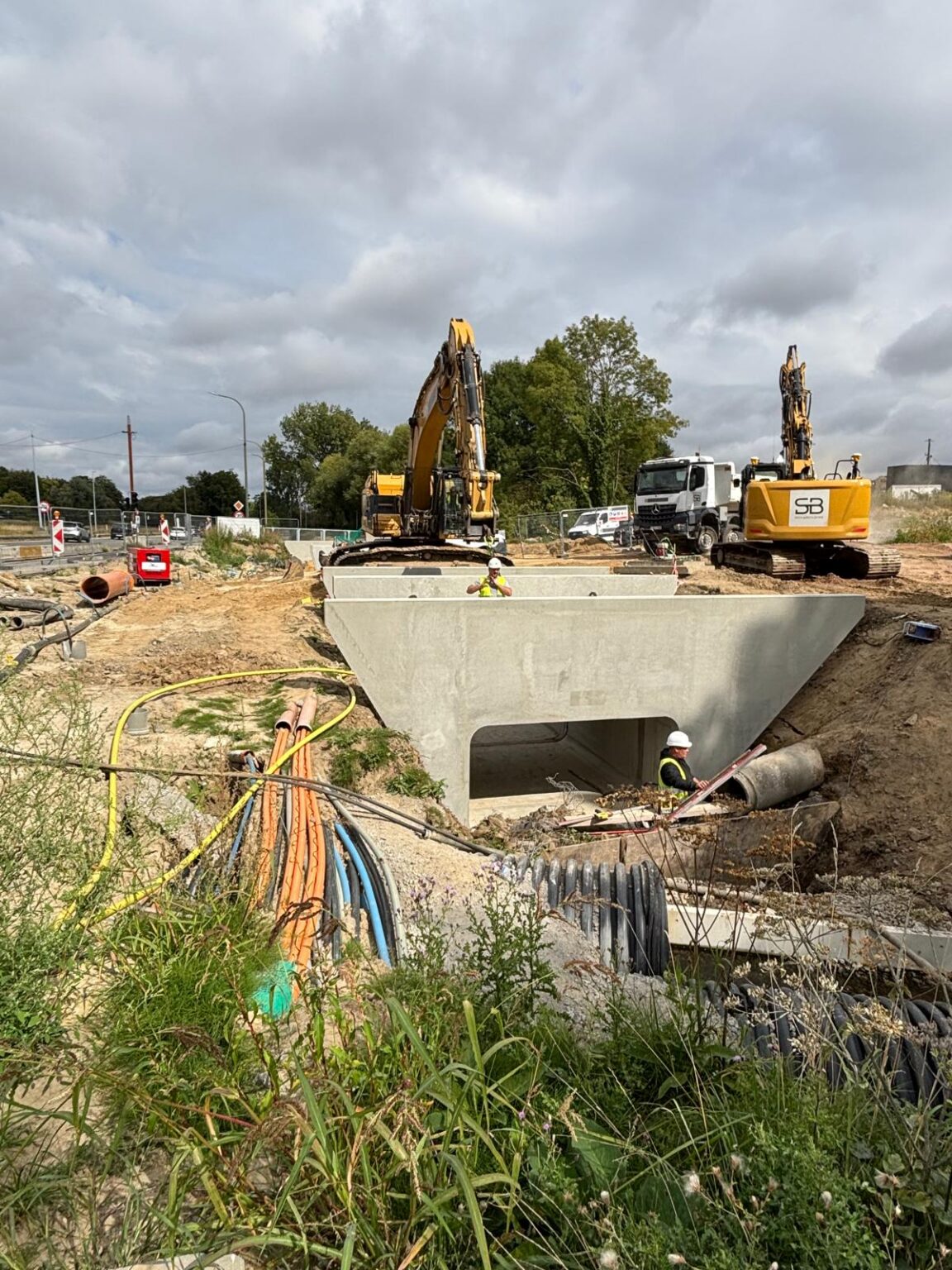 Nieuwe betonnen koker in de sleuf aan het kruispunt van de Grote Kloosterstraat en de R22, met graafmachines erachter