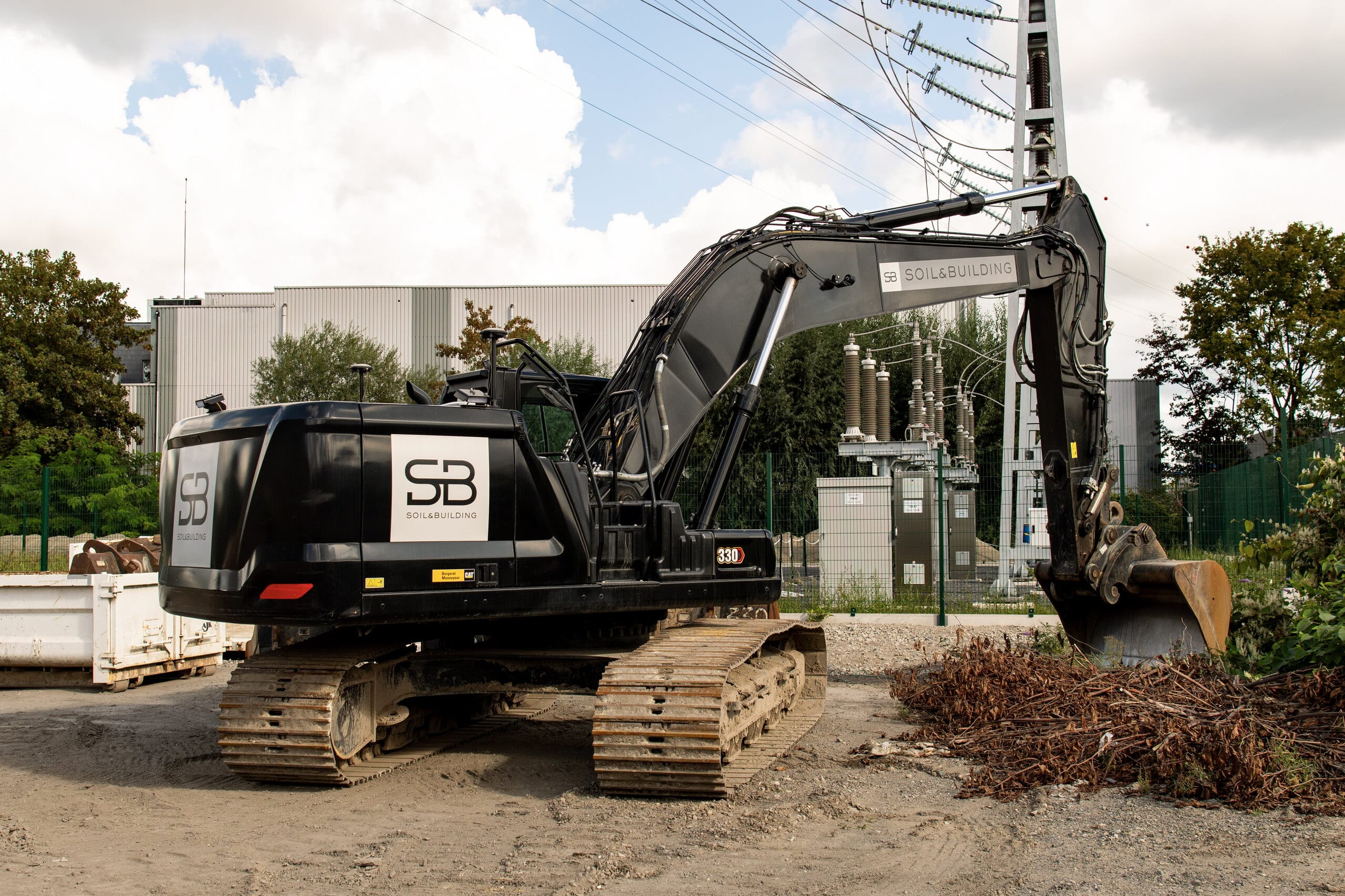 Zwarte rupsgraafmachine met het logo van Soil & Building op de werf