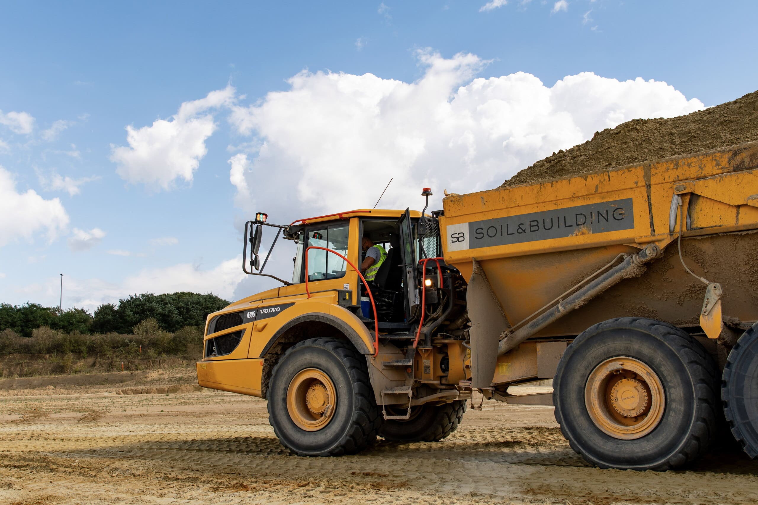 Knikdumper van Soil & Building met een lading zand op de werf