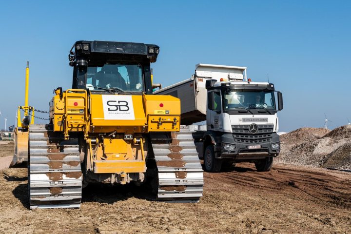 Gele bulldozer met Soil & Building-logo en een kipwagen op de werf van MG Park Big Bear in Evergem