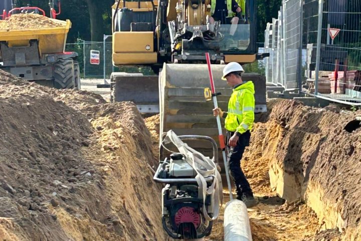 Arbeider verdicht de grond rond een rioleringsbuis in een sleuf op de werf van MG Park Venlo
